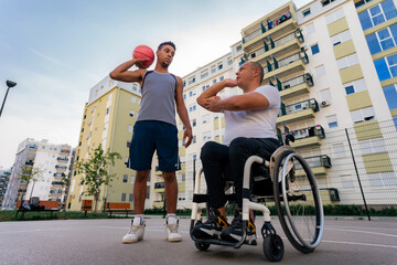 Mature man in the wheelchair coaching basketball to a young black man at the youth center before tryouts - Powered by Adobe