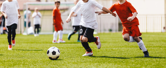 Children play soccer match. Anonymous football players kicking a ball. Two soccer teams compete in...