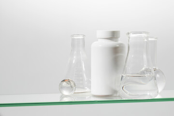 A white jar with vitamins or medicines with laboratory utensils on a glass shelf. Medicines