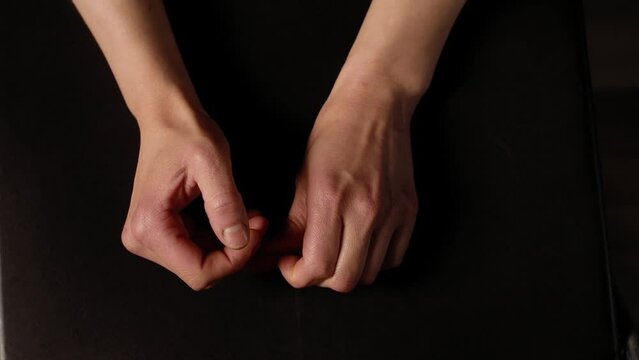 Close-up of male hands touching their nails due to stress against black background. Hand movements of a man under tension. Body language.
