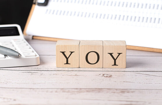 YOY - Year Over Year word on a wooden block with clipboard and calculator