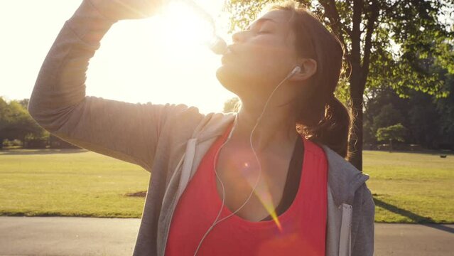 Woman, drinking water and hydrate on run in nature, liquid and nutrition for detox in outdoors. Female person, earphones and streaming music for workout, bottle and training for marathon in park