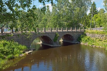 Fototapeta na wymiar Self-supporting old stone bridge with arches over river in summer.