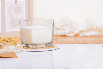 In a serene setting, a white candle stands elegantly on a clean white table, surrounded by artistic boho decorations