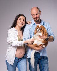 A pregnant woman in a white shirt, blue jeans with a bare belly and her husband are holding a...