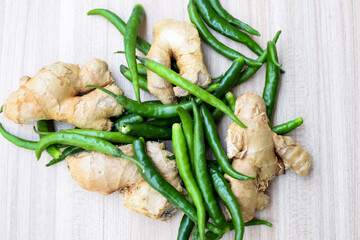 Fresh Ginger and green chili pepper on plain wooden table, green essential vegetables for all essential foods, view of unpeeled vegetables with plain background