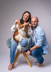 A pregnant woman with a bare belly sits on a blue armchair, holds a cocker spaniel in her arms and...