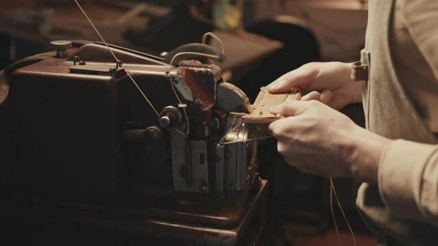 Hand of shoemaker using old-fashioned sewing machine for leatherwork in workshop