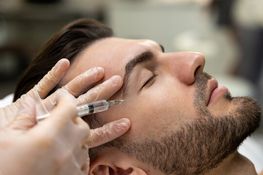 Dark-haired bearded man having session of mesotherapy in a beauty salon