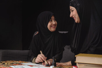 Muslim Arab woman teaching girl to write Arabic hand writing with ink, Arabic letters mean the name...