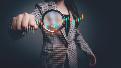 Businesswoman using magnifying glass focus to virtual financial graph chart icon about business...