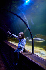 Young Girl Marvels at Sharks Swimming Above in Oceanarium Tunnel
