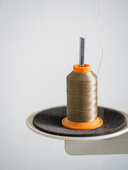 A spool of thread on the stand of a sewing machine on a white background.