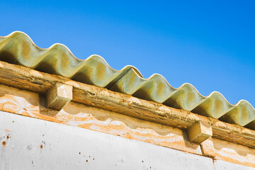 Old aged and damaged dangerous roof made of prefabricated and wave-shaped panels with wooden...