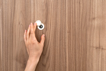 Woman hand opening peephole cover on wooden door