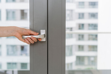 Cropped view of woman hand opening gray plastic door on balcony in apartment.