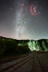 A breathtaking perspective of the Milky Way galaxy towering above a set of railroad tracks, with a...