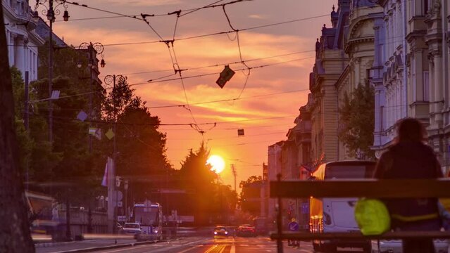Street with sunset in the Croatian capital Zagreb. People sitting on the bench near tree. Road traffic and tram rails