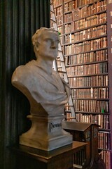 Trinity College library filled with books and featuring a bust of Sir Isaac Newton.