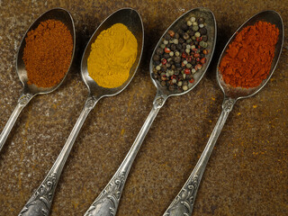 Old cupronickel spoons with various spices lie on an old metal table with traces of rust
