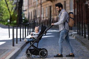 Dark-haired tall man with a baby carriage in the city street