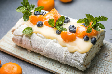 Meringue roll Pavlova cake with cream and fresh orange on top on a gray background. Copy space.