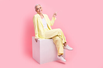 Full body photo of good mood person dressed yellow jacket indicating at promo empty space sit on...