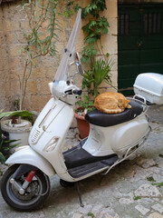 Uroczy rudy kot śpiący na siedzeniu skutera zaparkowanego na ulicy włoskiego miasta. A cute ginger cat sleeping on the seat of a scooter parked on the street of an Italian city. - obrazy, fototapety, plakaty