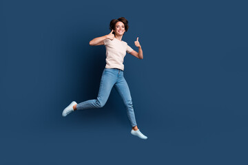 Fototapeta na wymiar Full length photo of lovely young lady jump run show double thumb up wear trendy white garment isolated on dark blue color background