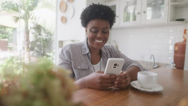 Happy black woman with short hair watching video and photos on mobile smart phone in the kitchen 