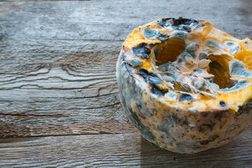 Orange moldy pumpkin on a wooden background. Mold and fungi on food, mold development, pests of stored vegetable products, a common problem.