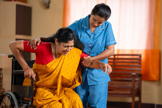 Nurse helping woman to getup from wheelchair during training or therapy session - concept of rehabilitation, professional caring, medical support
