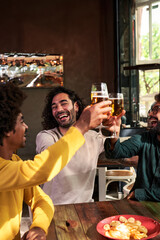 Multiethnic group of three men friends toasting with beers at a bar cheerfully. Celebrating and gathering together during the day. Vertical image with copy space.