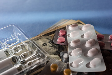 Vaccine bottles and medical pills on blue surface with dollar banknotes