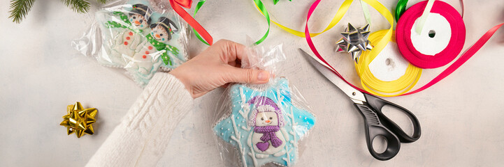 banner of female hands are packing Christmas gifts with gingerbread with snowmen on a gray background with scissors, colorful ribbons, bows. soft focus. flat lay