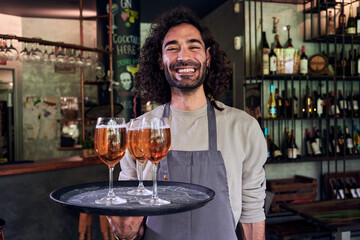 Portrait of a happy waiter looking at camera smiling while holding a tray with beers at his workplace. Copy space photo.