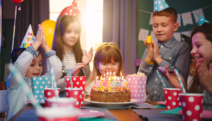 Birthday party of small Caucasian girl blowing candles on the cake and her small friends applauding...