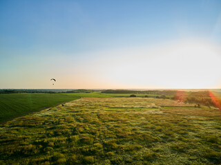 Paraglider Soaring High Above Lush Green Fields on a Sunny Day