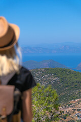 Fototapeta na wymiar Beautiful view of the sea and mountains on a sunny summer day, in the foreground is out of focus a young female tourist in a hat with a backpack. Concept of travel, tourism.