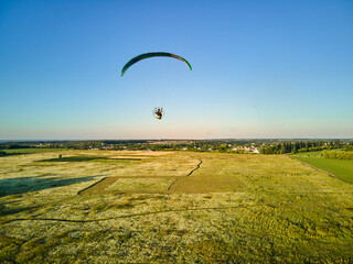 Paraglider Soaring High Above Lush Green Fields on a Sunny Day