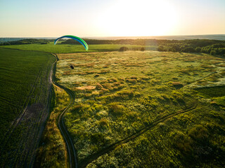 Paraglider Soaring High Above Lush Green Fields on a Sunny Day