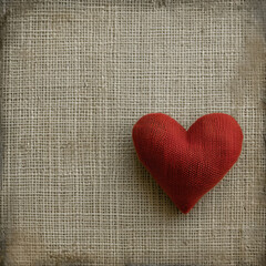 A textured burlap background with a single red fabric heart placed in the lower right corner.