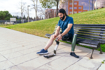 Sportive man fitting his carbon fiber prosthetic leg on a sunny day at the park, preparing for a running session.