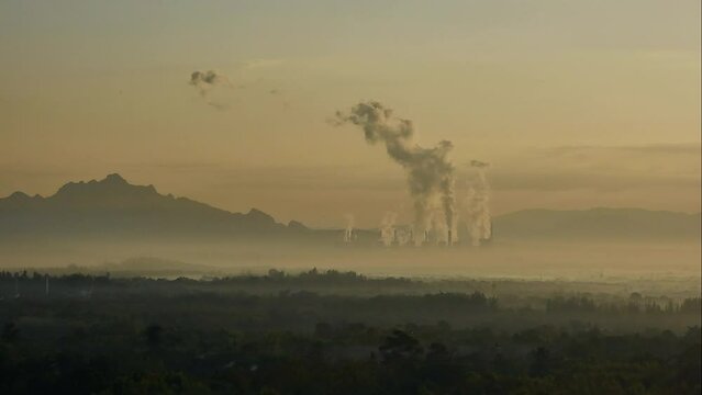 The atmosphere is tainted by air pollution as smoke and smog envelop the landscape, emanating from industrial activities, particularly a coal power plant in the morning mist