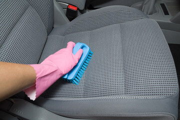 Woman hand in rubber protective glove holding brush and cleaning gray textile car seat. Care about auto interior. Point of view shot. - obrazy, fototapety, plakaty