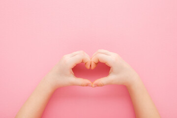 Heart shape created from little girl hands on light pink table background. Pastel color. Love, health and hope concept. Closeup. Point of view shot. Top down view. - obrazy, fototapety, plakaty
