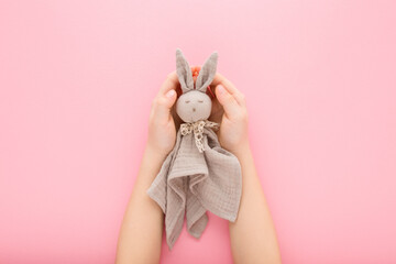 Little girl hands holding light gray cloth bunny toy on light pink table background. Pastel color....