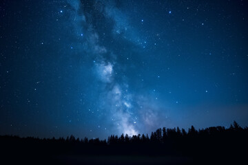 Blue dark night sky with many stars above field of trees. Milkyway cosmos background