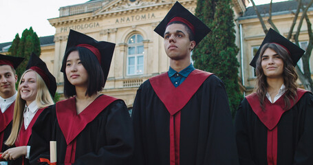 Portrait shot of the young happy multiethnic students in academic caps and gowns and with diplomas...