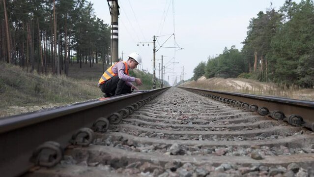 A railway worker inspects the tracks, takes measurements with a tape measure and writes down the calculations in a journal.